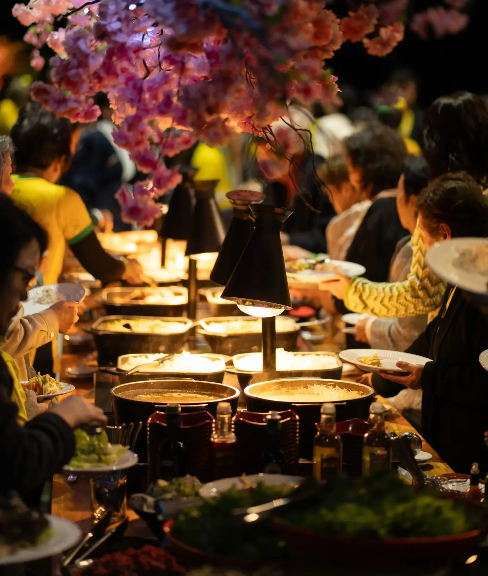 Pessoas se servindo no buffet sob flores decorativas e luzes, em foto de divulgação do Costão Matsuri 2027.